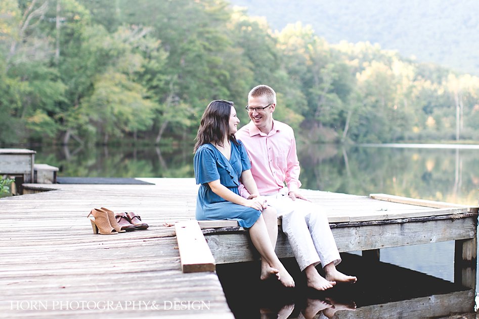 adventure engagement session, couple sits on dock beside lake with shoes off