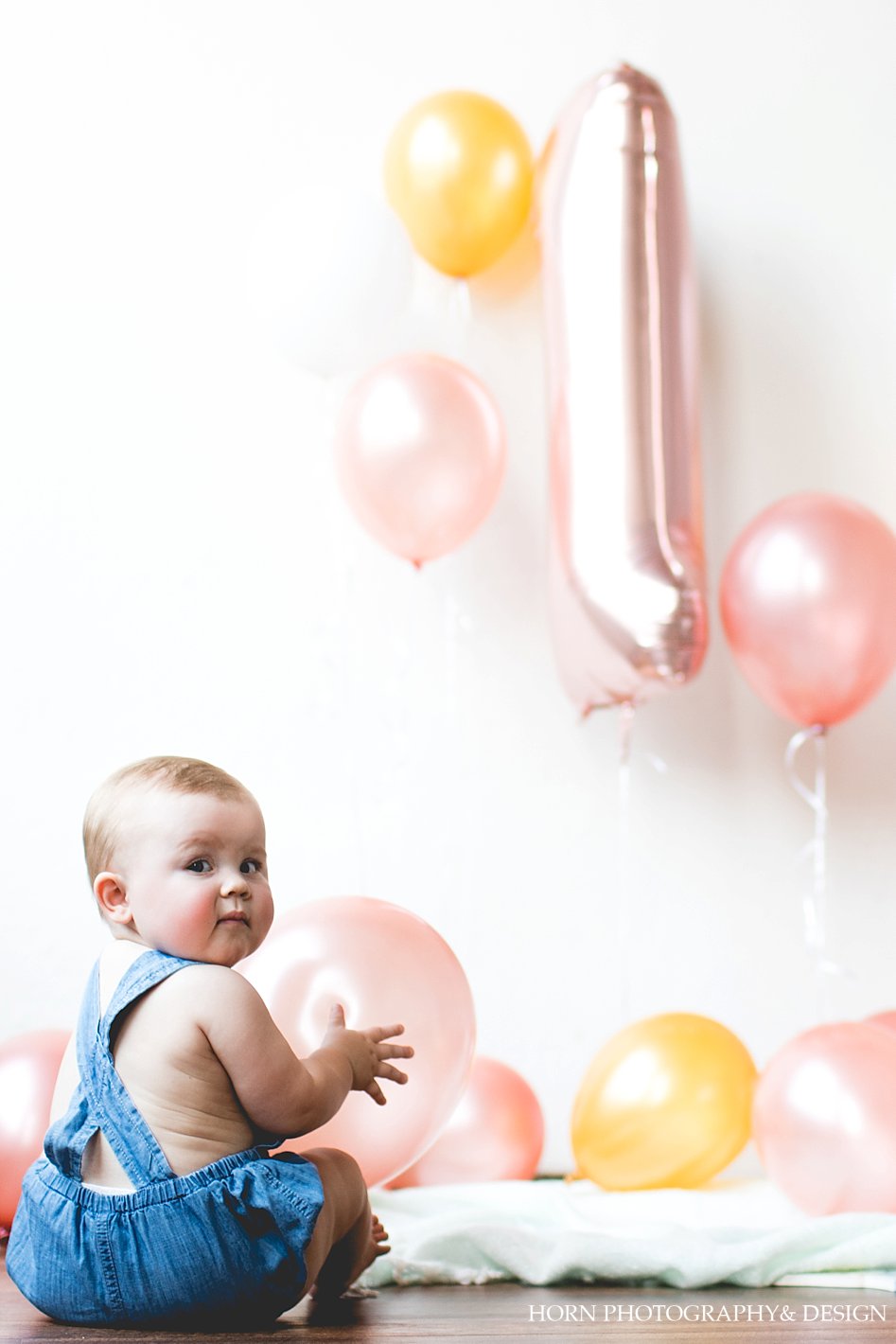 cute chubby baby looking back with number one pink balloon in background
