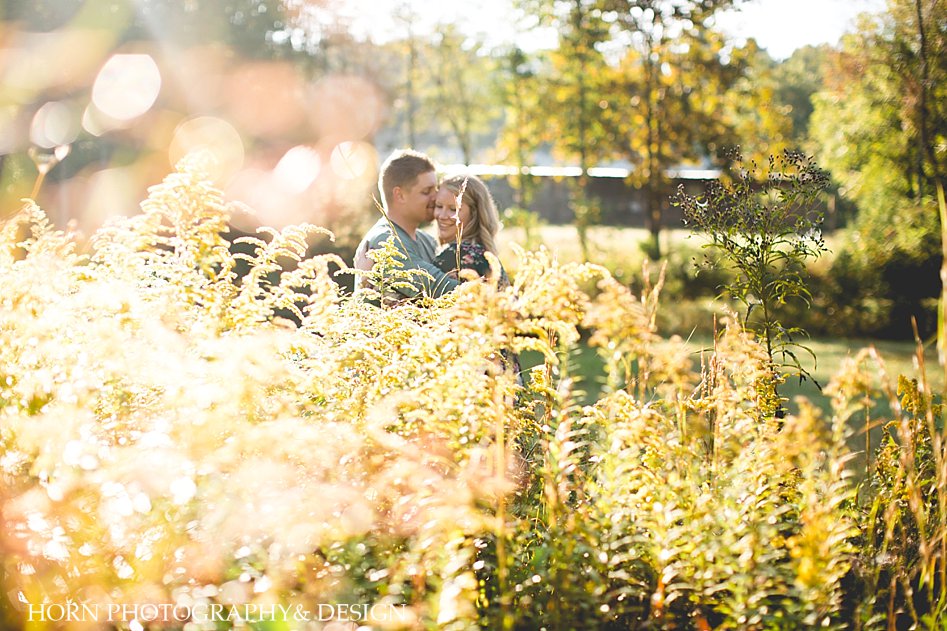 couple holds one another during engagement session with sun flare from the top