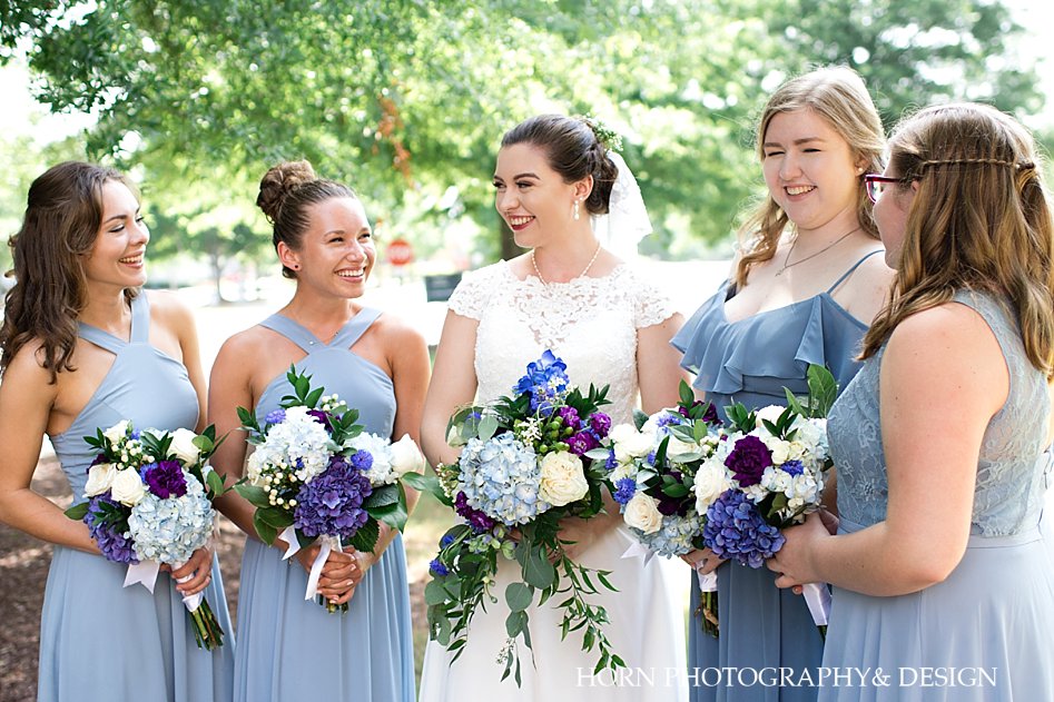 bride and bridesmaids laughing and chatting purple blue  hydrangea white roses eucalyptus leaves bouquet horn photography and design