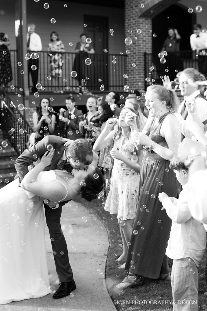black and white groom dipping and kissing bride in bubble parade leaving reception the beginning of forever horn photography and design