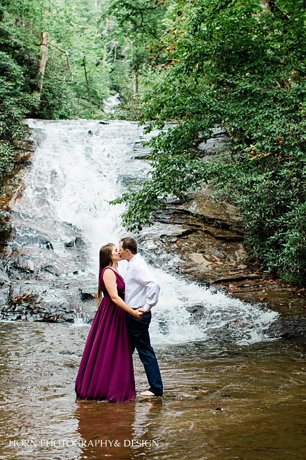 couple kissing during Appalachian Waterfall Engagement session standing in front of waterfall in the water