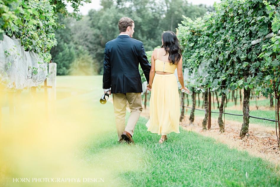 engaged couple walks away in vineyard